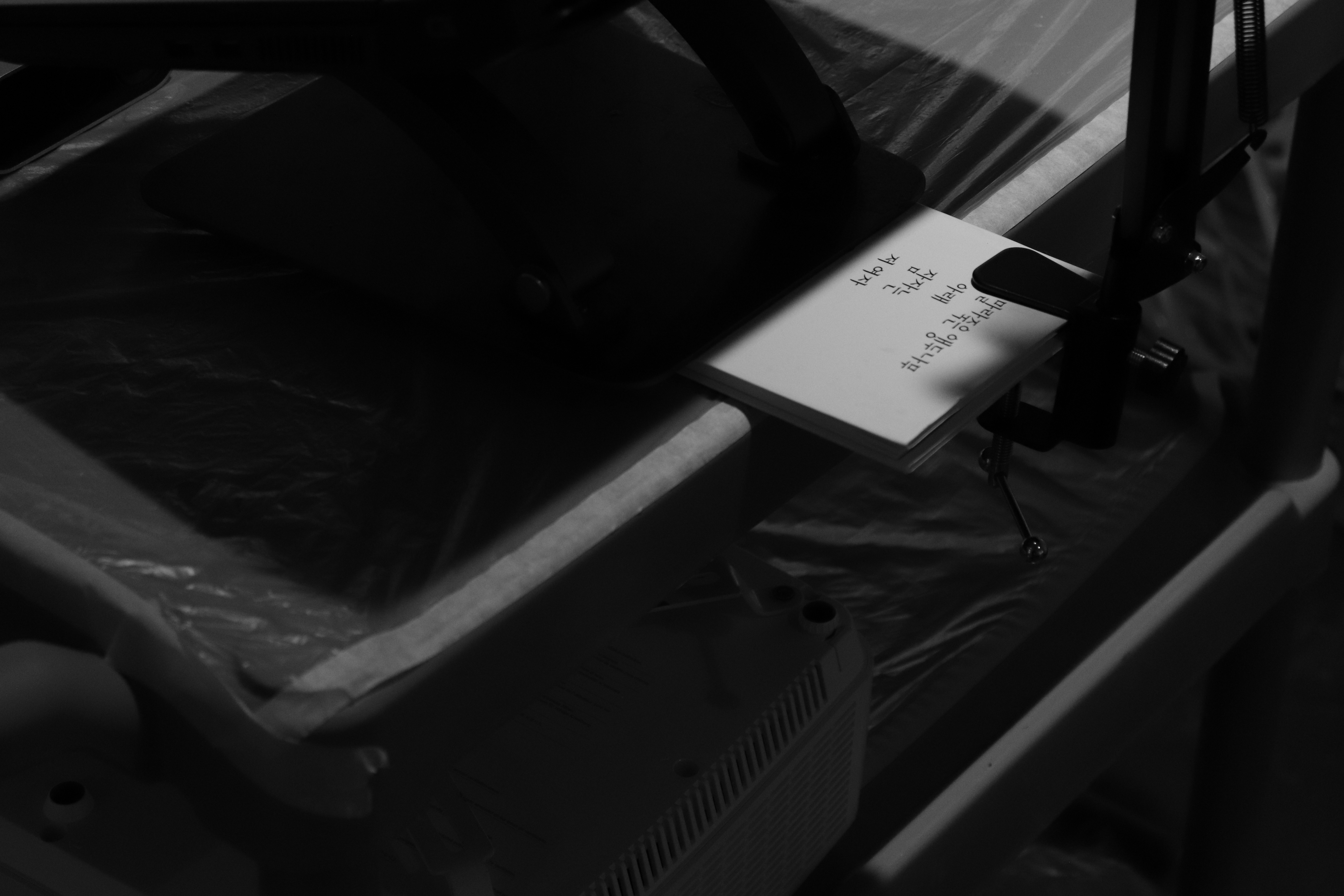 김언희의 시집'말라죽은 앵두나무 아래 잠자는 저 여자'가 카메라 클램프를 고정하는 용도로 노트북 스탠드 아래에 고정되어 있다. 흑백사진.